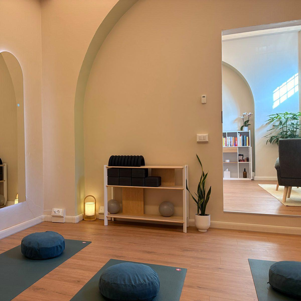 The sage-painted arch in the practice room, with the rack of blocks and Pilates balls and a doorway through to the sunlit reception