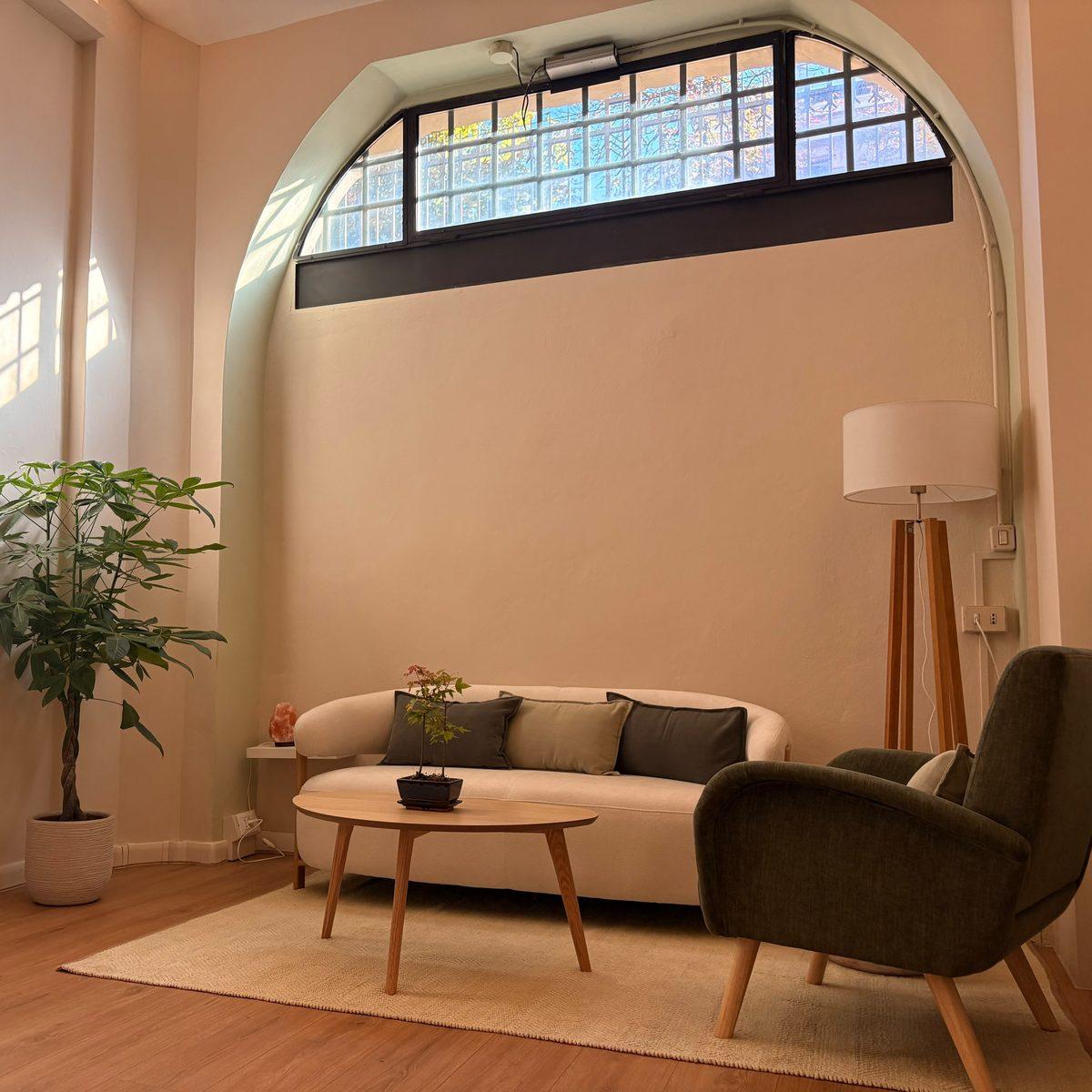 Kala's reception: a curved cream sofa, green armchair and oak table beneath the tall arched window